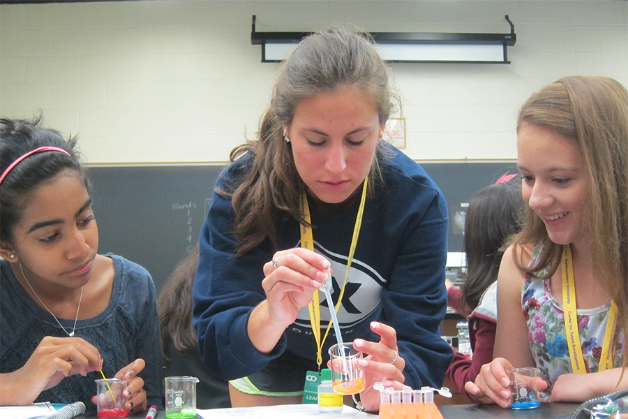 two girls with teacher in the middle doing an experiment